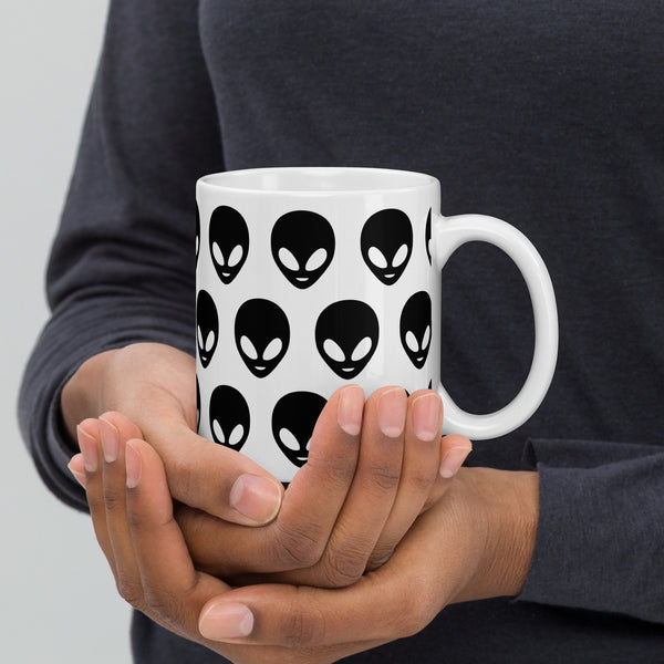 Person holding a white mug with black alien face patterns against a gray background