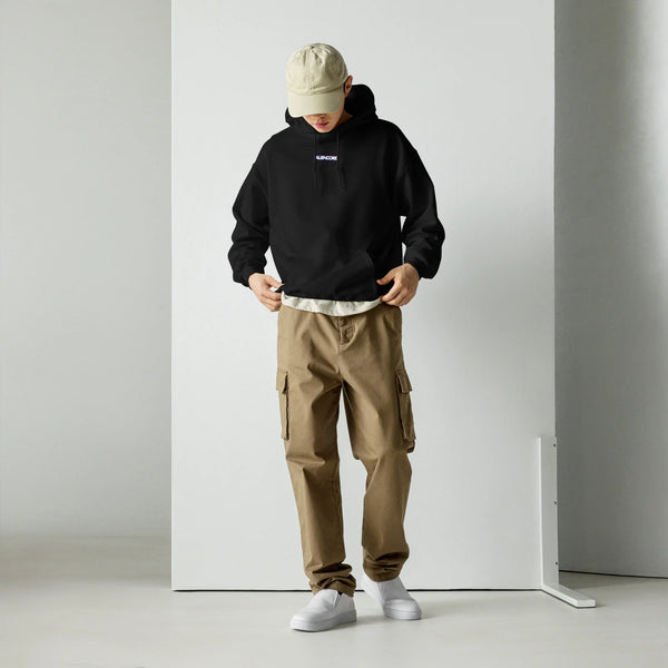 Person wearing a black hoodie, beige cap, and brown cargo pants against a white background