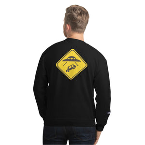 Person wearing a black sweatshirt with a yellow UFO sign on the back against a white brick wall.