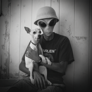 Person wearing an alien helmet holding a dog against a wooden wall.